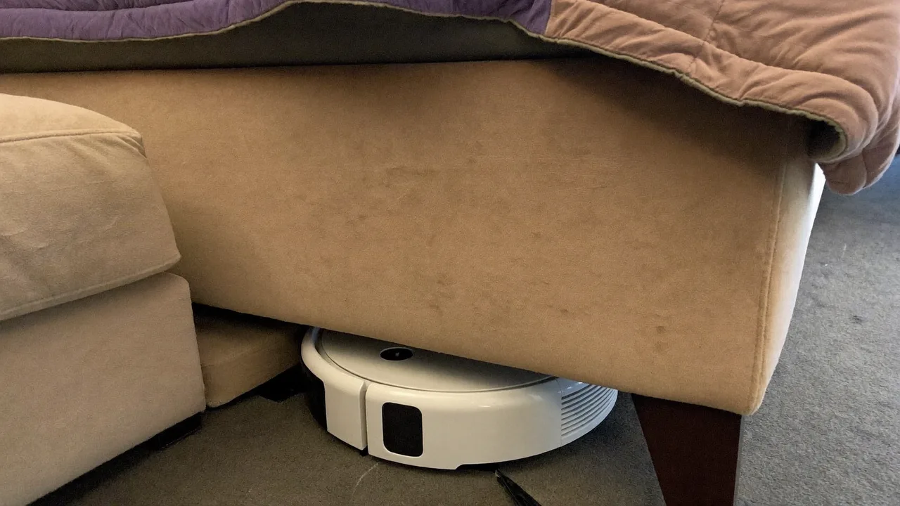 薄型のロボット掃除機がソファの下の狭い隙間に入り込んで掃除している様子